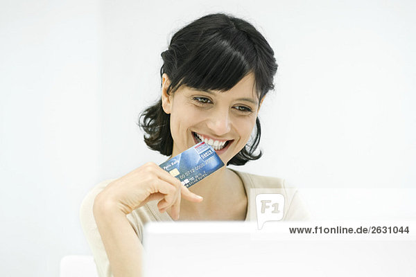 Frau beißt Kante der Kreditkarte  lächelnd auf Laptop
