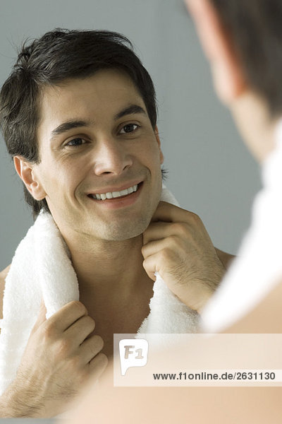 Mann schaut sich selbst im Spiegel an  lächelt  hält ein Handtuch auf den Schultern.