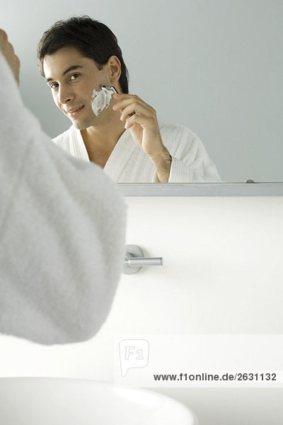 Der Mann schaut sich im Spiegel an  rasiert sich  trägt einen Bademantel.