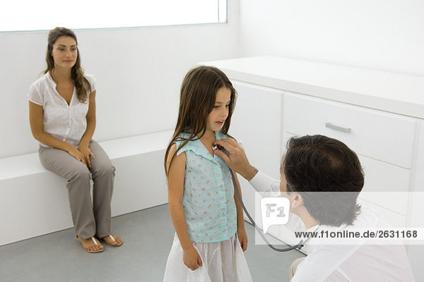 Kinderarzt hält Stethoskop an Mädchenbrust  Mutter sitzt in der Nähe