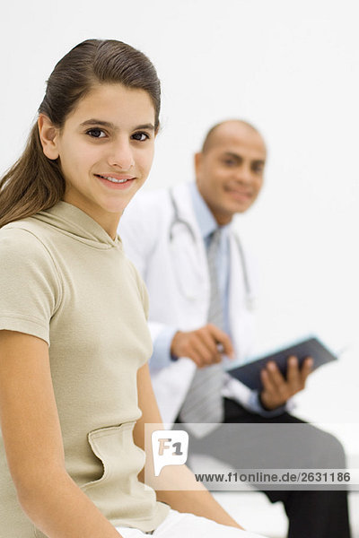 Teenagermädchen lächelt in die Kamera  Arzt hält Mappe im Hintergrund