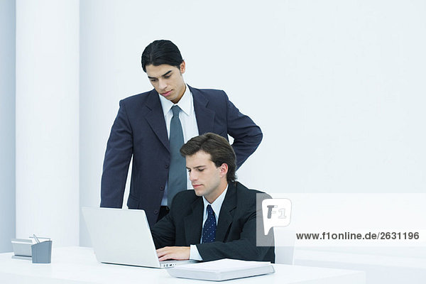 Businessman using laptop computer at desk  colleague watching over his shoulder
