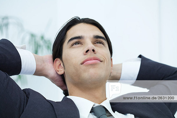 Young businessman leaning back with hands behind head  looking up  portrait