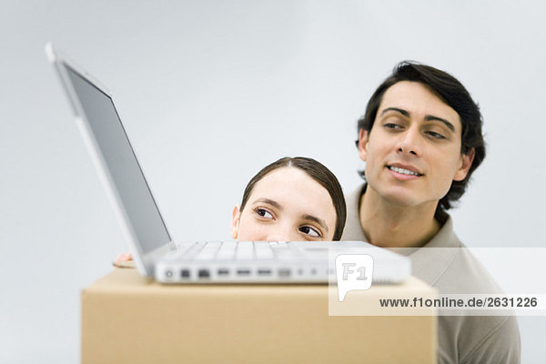 Mann und Frau schauen auf einen Laptop  der auf einem Karton sitzt.
