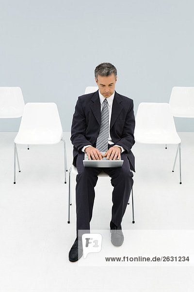 Businessman sitting in chair using laptop  empty chairs in background