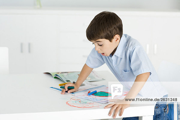 Boy leaning on table  holding crayon  colorful drawing on paper and table