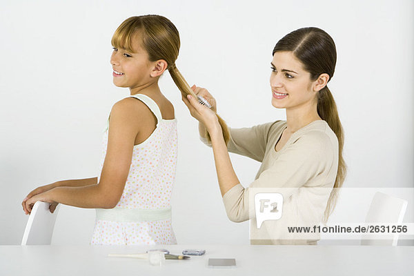 Young woman combing her younger sister's hair  side view