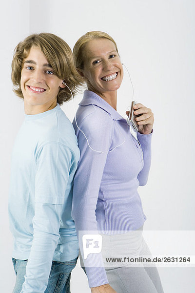 Mutter und jugendlicher Sohn hören zusammen MP3-Player  stehen Rücken an Rücken  lächeln vor der Kamera