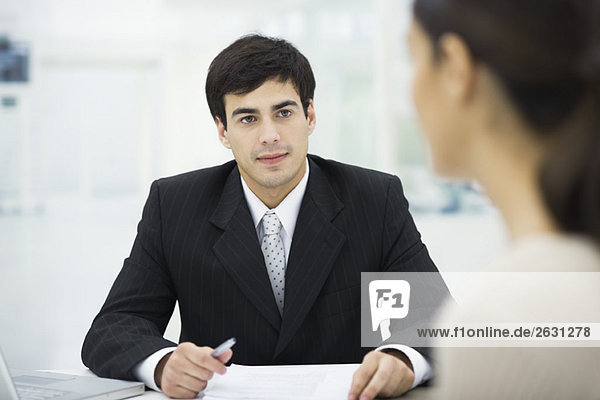 Businessman sitting at desk  listening to female client