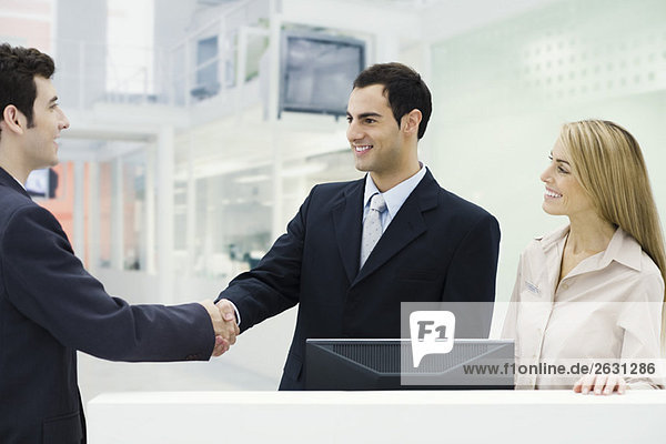 Three professionals standing at counter  men shaking hands