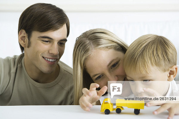 Kleiner Junge spielt mit Spielzeugauto  Eltern schauen lächelnd zu