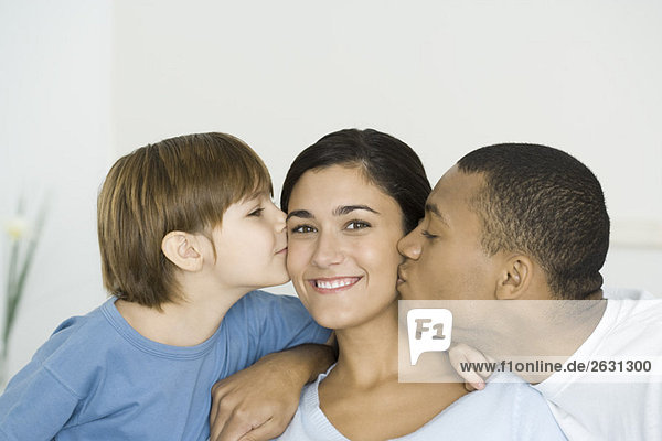 Mann und Sohn küssen die Wangen der Frau  Frau lächelt in die Kamera.
