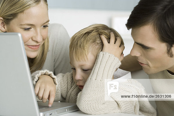 Parents helping little boy use laptop computer  close-up