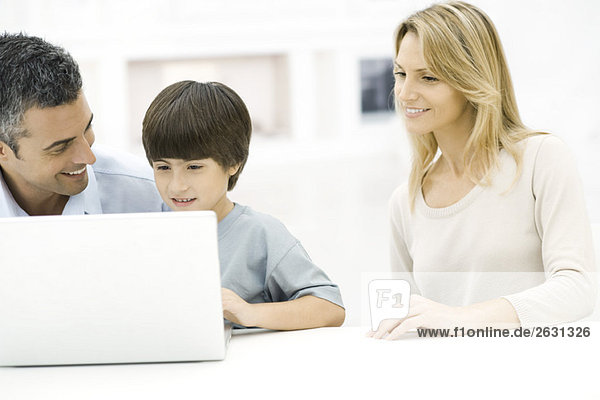 Father and son using laptop computer together  mother watching