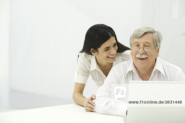 Senior Mann und mittlere erwachsene Frau  die zusammen auf den Laptop schauen  lächelnd