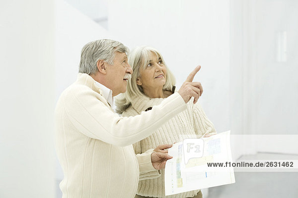 Seniorenpaar steht zusammen  Mann hält Grundrisse und zeigt nach oben