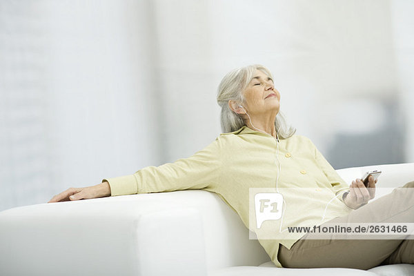 Seniorenfrau beim Musikhören  auf der Couch sitzend mit geschlossenen Augen