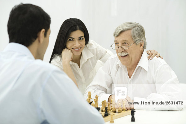 Menschen spielen Schach  Frau sitzt mit der Hand auf der Schulter des älteren Mannes.