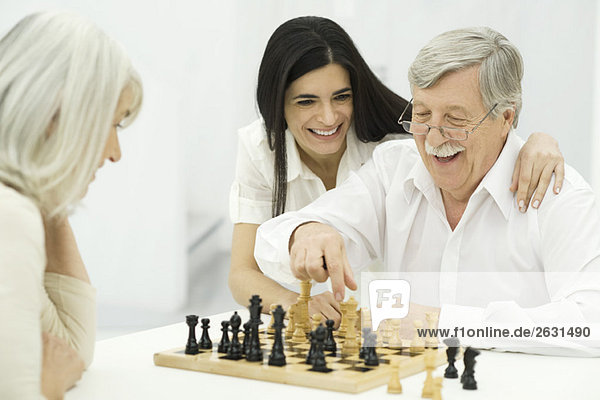 Seniorenpaar beim Schachspielen  erwachsene Tochter mit Arm um Vater sitzend