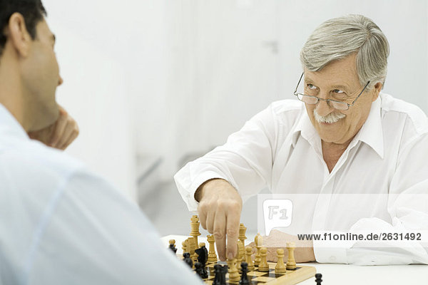 Father playing chess with adult son  smirking