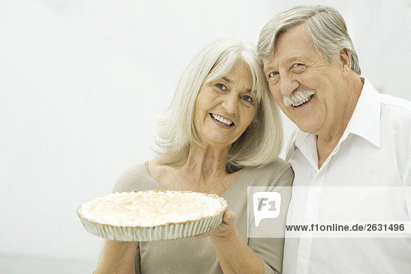 Seniorenpaar lächelt  Frau hält Kuchen hoch