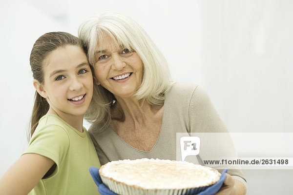Grandmother and granddaughter smiling at camera  woman holding pie
