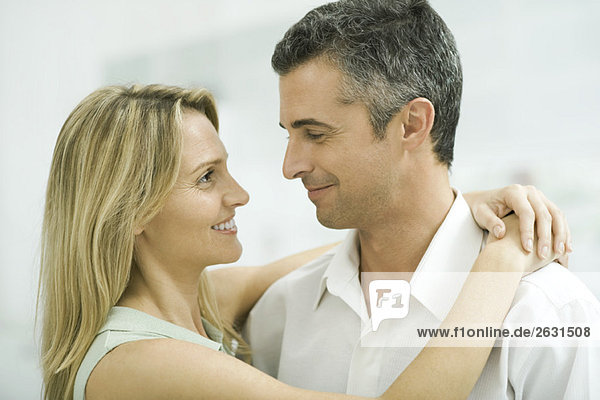 Ein Paar lächelt sich an  eine Frau wickelt die Arme um den Mann.
