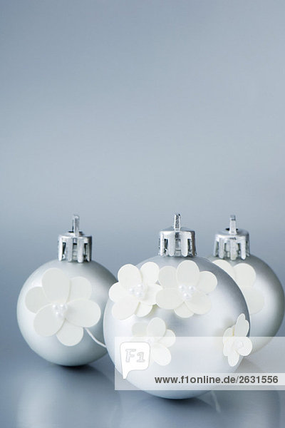 Three silver Christmas tree ornaments decorated with white flowers