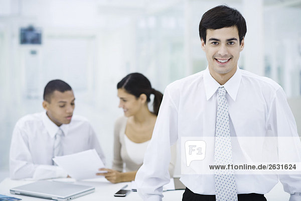 Businessman smiling at camera  colleagues working in background