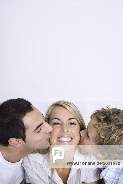 Woman being kissed on cheeks by husband and son  smiling  portrait