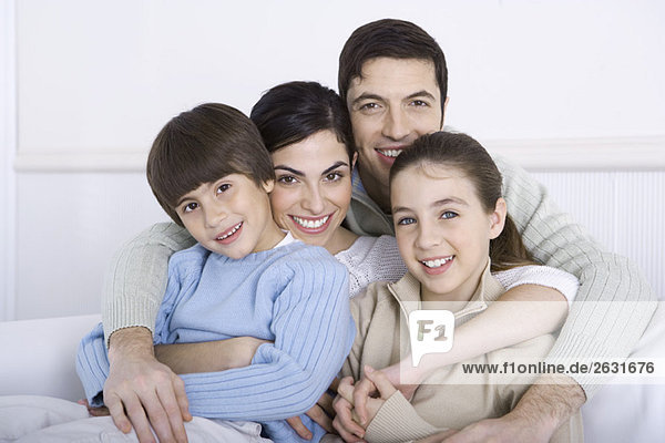 Vater umarmt seine Frau und zwei Kinder  alle lächelnd vor der Kamera.