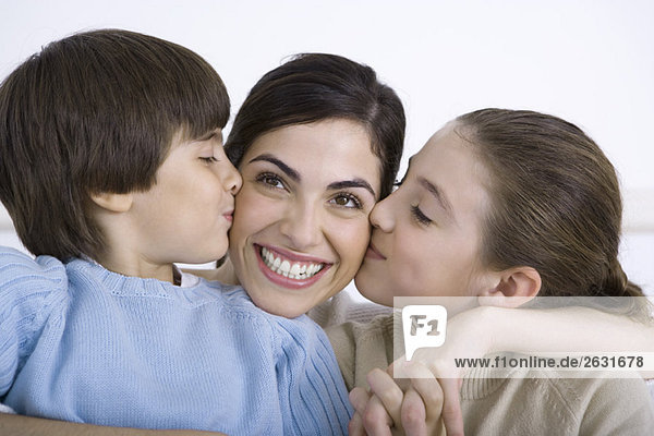 Mother being kissed on each cheek by young daughter and son  smiling