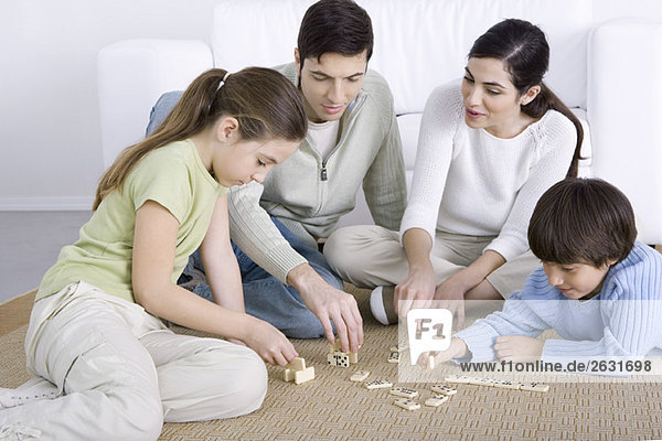 Parents and two children seated on floor  playing dominoes together