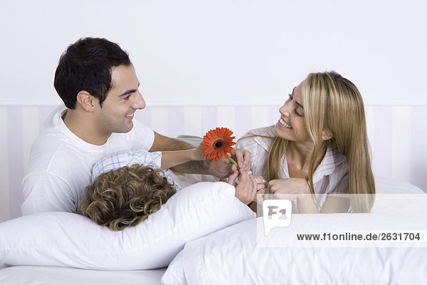 Familie zusammen im Bett liegend  Vater und Sohn schenken Mutter eine Blume