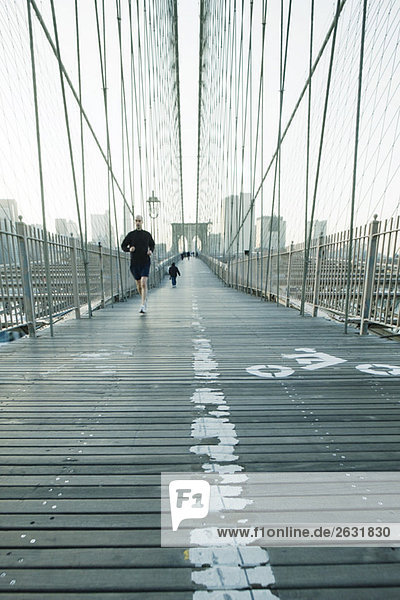Jogger läuft über den Fußgängerweg der Brooklyn Bridge in New York City  Manhattan Skyline in der Ferne.