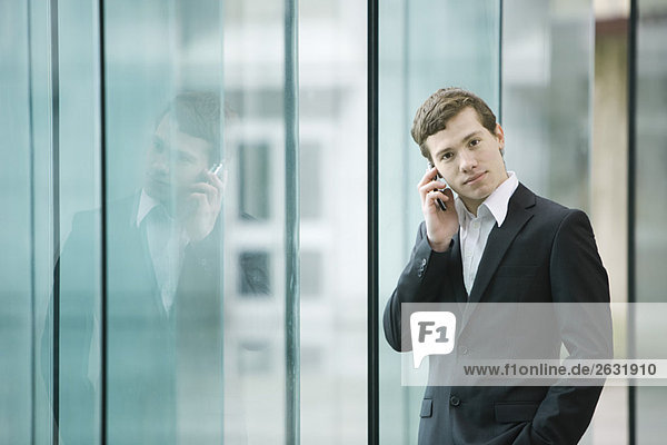 Geschäftsmann steht an der Glaswand und telefoniert mit dem Handy