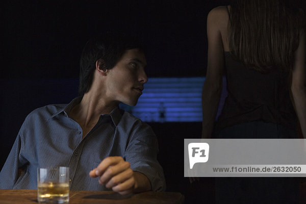 Glas Whiskey auf dem Tisch  Mann sitzt und schaut weg  Rückansicht der Frau im Dunkeln stehend