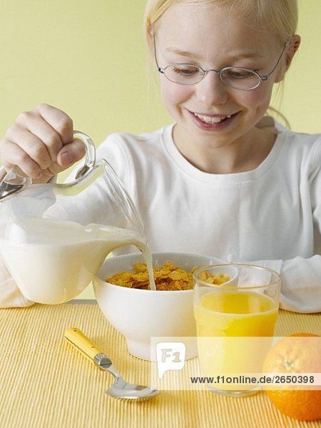 Mädchen giesst sich Milch über Cornflakes