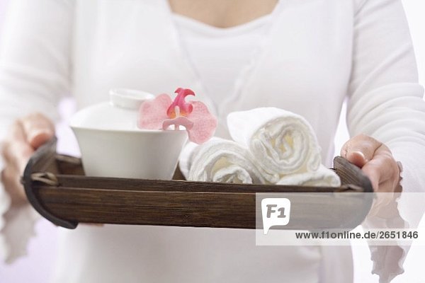 Frau hält Tablett mit Handtüchern  Schale und Orchidee