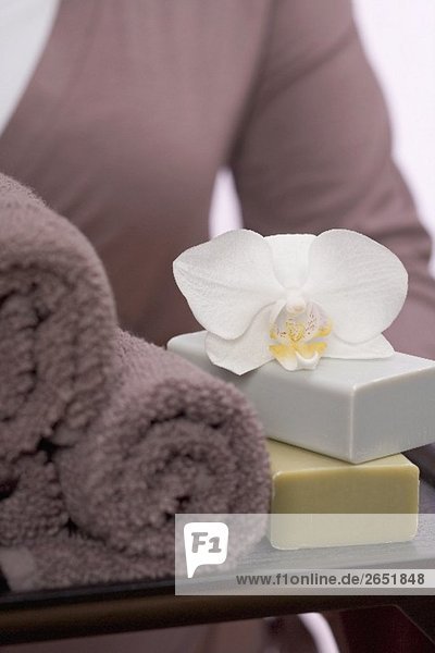 Frau hält Tablett mit Handtüchern  Seifen und Orchidee