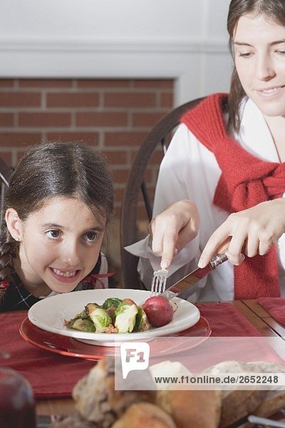 Young woman cutting up vegetables on small girl's plate