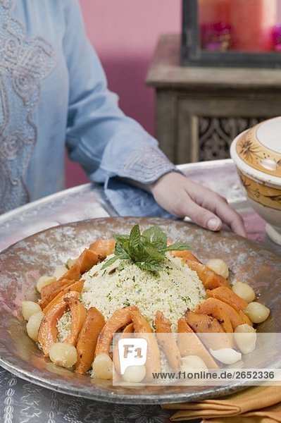 Frau serviert Couscous mit Kürbis  Minze und Zwiebeln