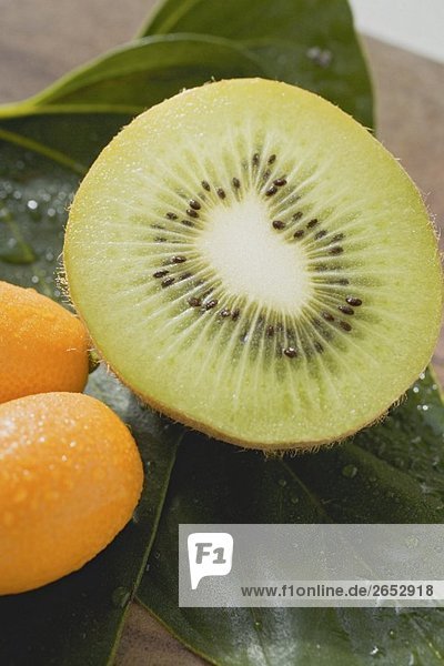 Halbe Kiwi und zwei Kumquats auf Blättern