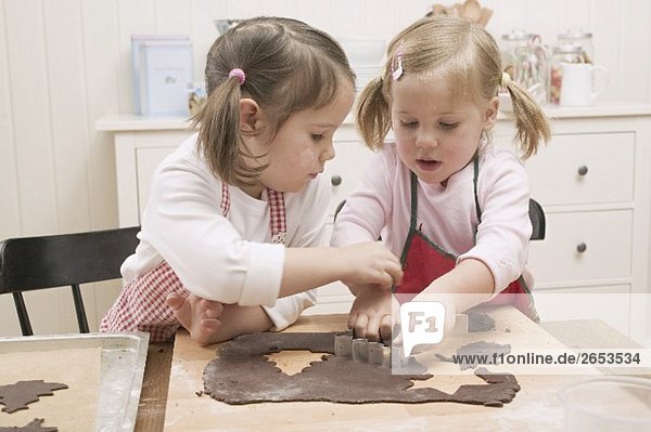 Zwei kleine Mädchen stechen Schokoladenplätzchen aus