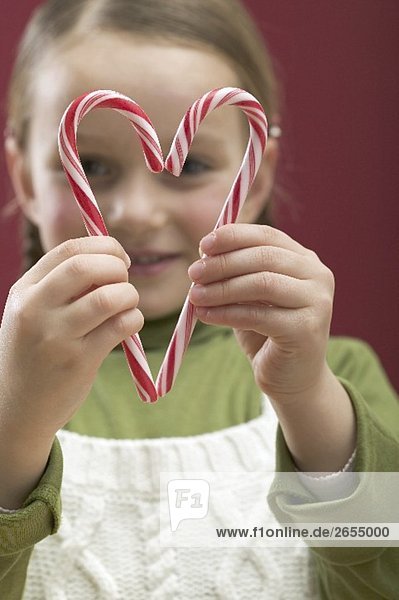 Kleines Mädchen schaut durch Herz aus Zuckerstangen