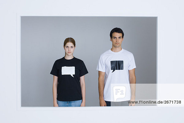 Junger Mann und junge Frau in T-Shirts  bedruckt mit leeren Wortblasen  mit Blick auf die Kamera.