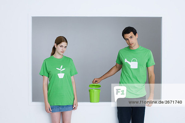 Junge Erwachsene in T-Shirts  bedruckt mit Gießkanne und Topfpflanze  Mann öffnet kleine Mülltonne