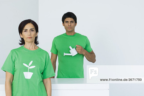 Frau im T-Shirt mit Pflanzengrafik  Mann mit Gießkanne im Hintergrund