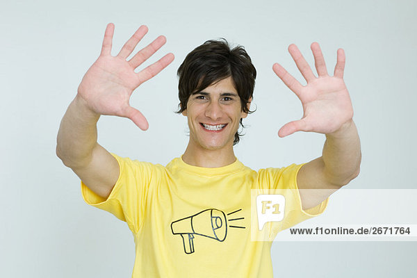 Junger Mann im T-Shirt mit Megaphon-Grafik  lächelnd in die Kamera  Hände erhoben