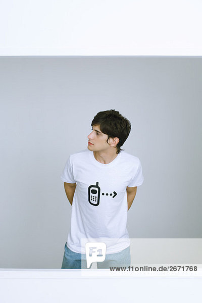 Junger Mann im T-Shirt mit Handy-Grafik  wegschauend  Hände hinter dem Rücken